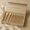 Set of gold makeup brushes in a 'Aura Beauty' box on a beige fabric background